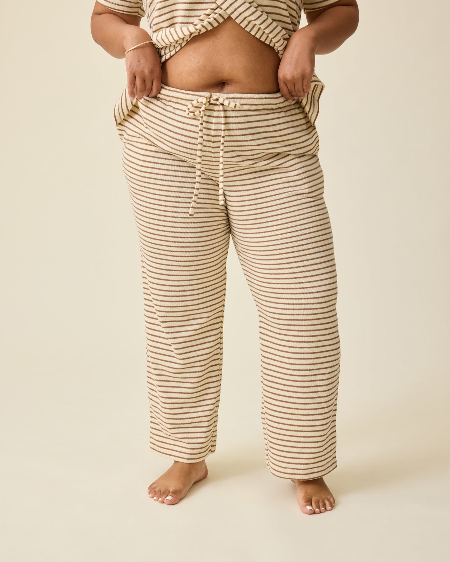 Model is lifting up the breastfeeding flap for access on Luxe Terry Maternity & Nursing Split Hem T-shirt in Ivory & Chocolate Stripe and Luxe Terry Maternity & Postpartum Pant in Ivory & Chocolate Stripe, on a beige background.@model_info:Brittany is 5'5" and wearing an X-Large.