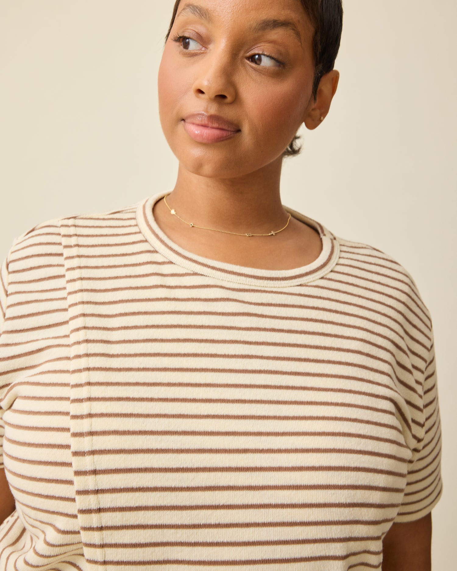 Model is wearing Luxe Terry Maternity & Nursing Split Hem T-shirt in Ivory & Chocolate Stripe on a beige background.