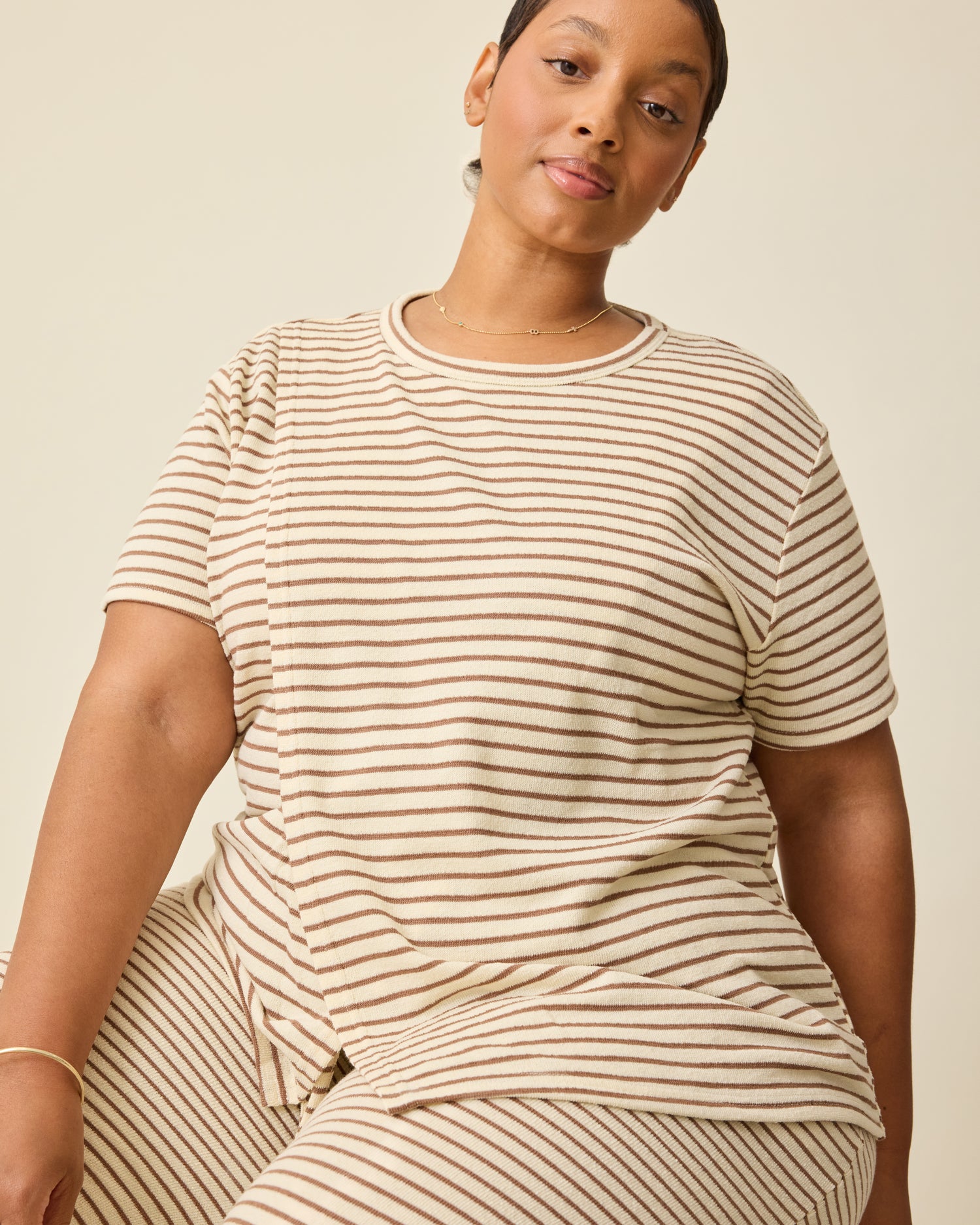 Model is wearing Luxe Terry Maternity & Nursing Split Hem T-shirt in Ivory & Chocolate Stripe and Luxe Terry Maternity & Postpartum Pant in Ivory & Chocolate Stripe, on a beige background. @model_info:Brittany is wearing an X-Large.