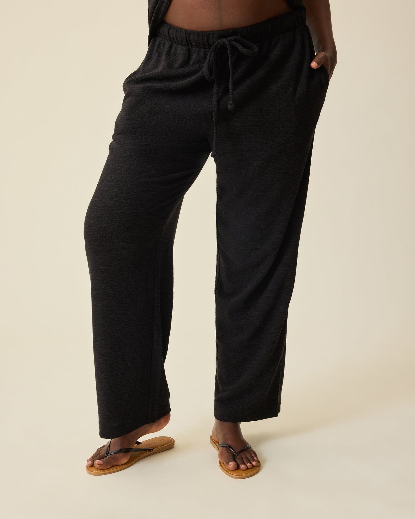 Model is wearing Luxe Terry Maternity & Postpartum Pant in Black, on a beige background.@model_info:Anna is 5'8.5" and wearing a Large.