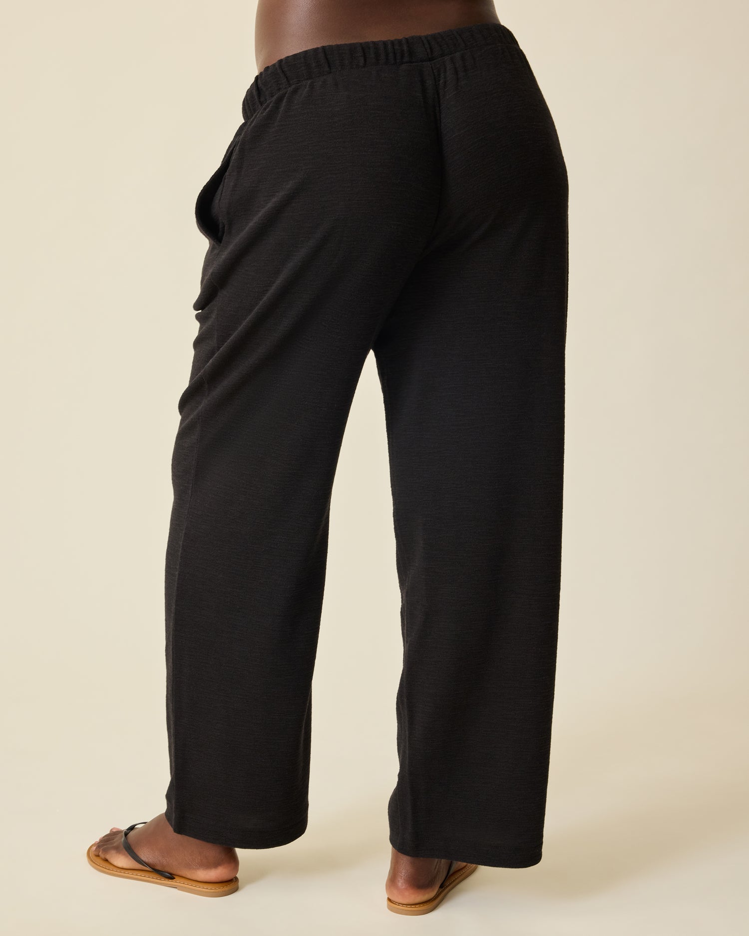 Back view of Model wearing Luxe Terry Maternity & Postpartum Pant in Black, on a beige background.