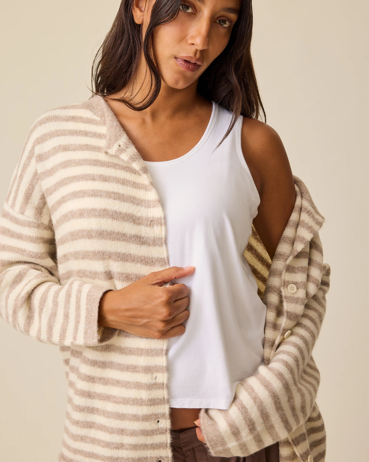 Model is has one shoulder bared with Ultra Soft Maternity & Postpartum Cardigan in Tan & White Stripe, Maternity & Postpartum Wide Leg Trouser in Brown and a nursing white tank, on a beige background.
