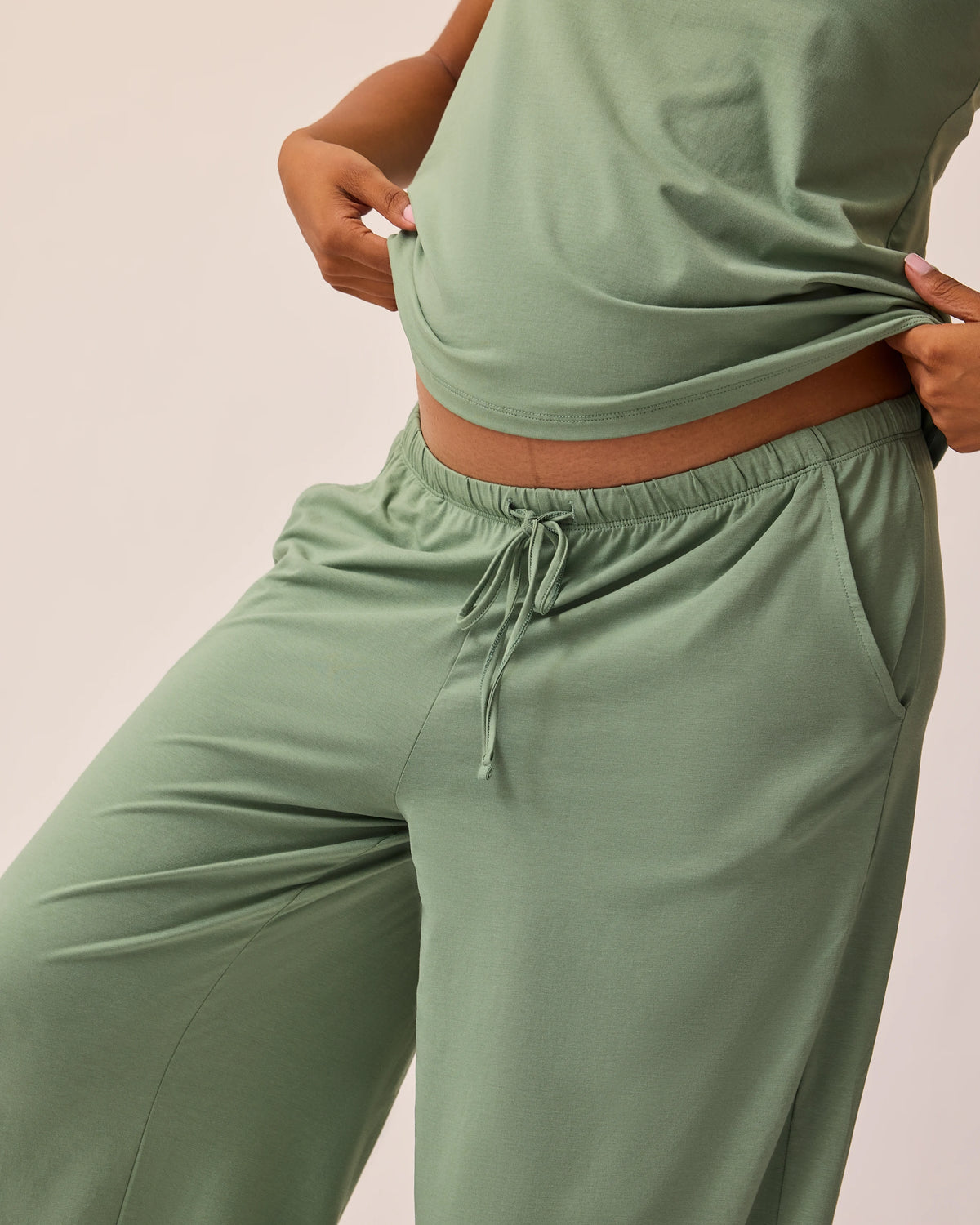 Angled view of model wearing pants and tank of the Maternity & Nursing Three-Piece Pajama Set in Sage on a beige background.