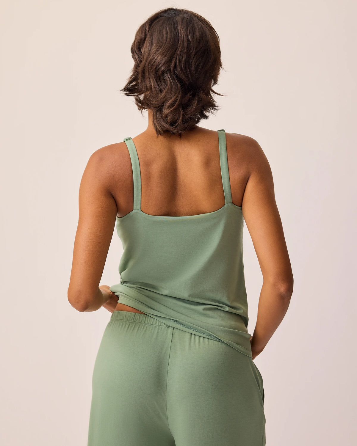 Back view of model wearing pants and tank of the Maternity & Nursing Three-Piece Pajama Set in Sage on a beige background.