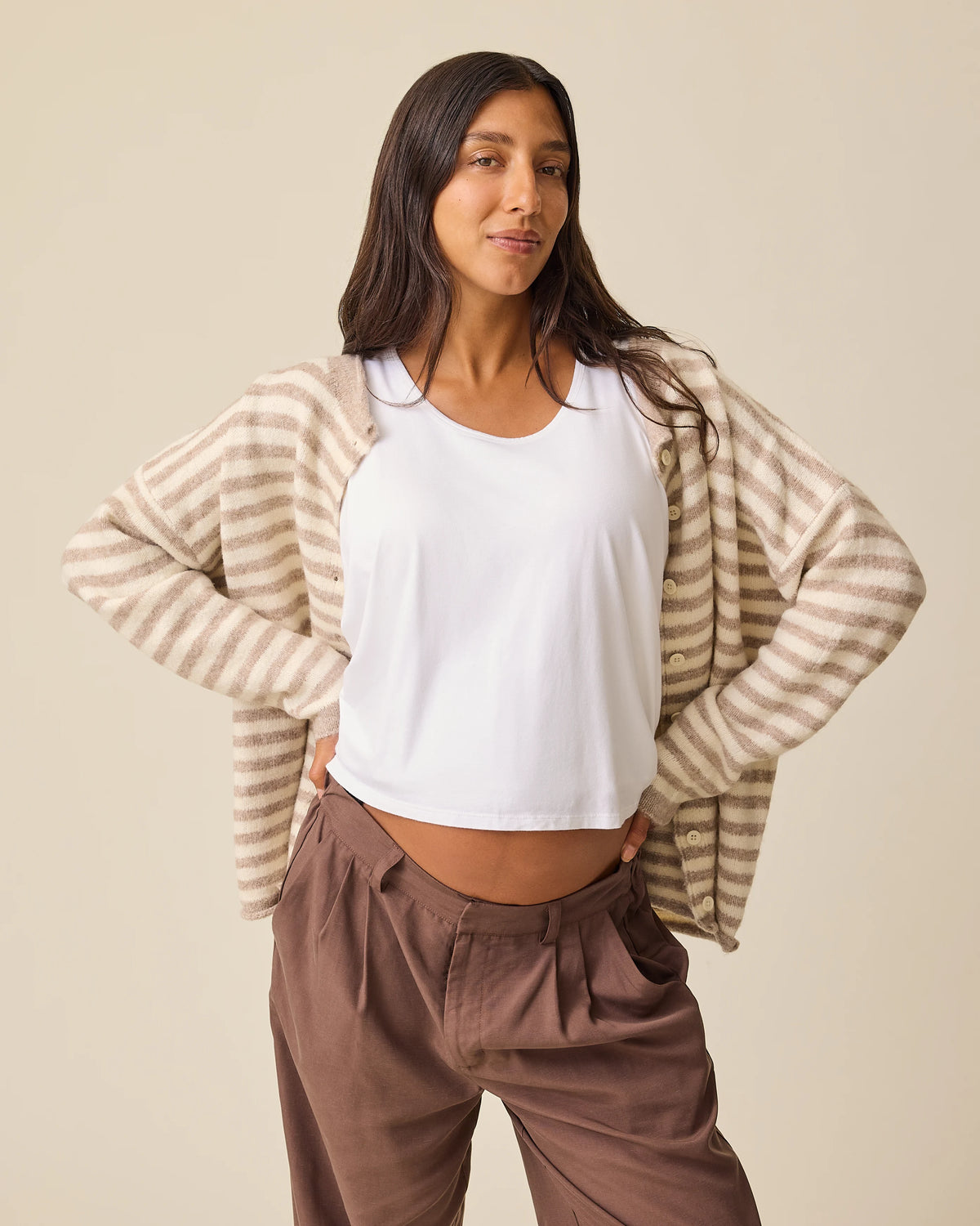 Model is baring baby bump under Ultra Soft Maternity & Postpartum Cardigan in Tan & White Stripe, Maternity & Postpartum Wide Leg Trouser in Brown and a nursing white tee, on a beige background.