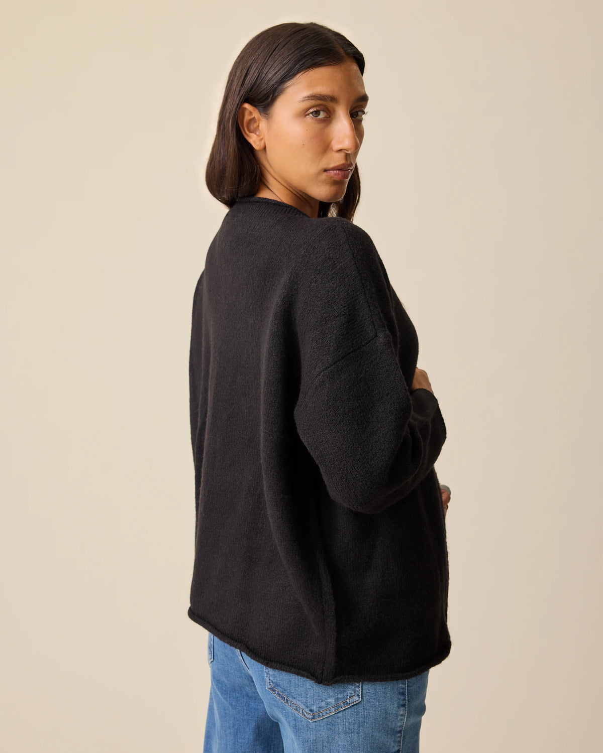 Back view of the model wearing Ultra Soft Maternity & Postpartum Cardigan in Black, Wide Leg Maternity & Postpartum Jean in Medium Wash and a white nursing top, on a beige background.