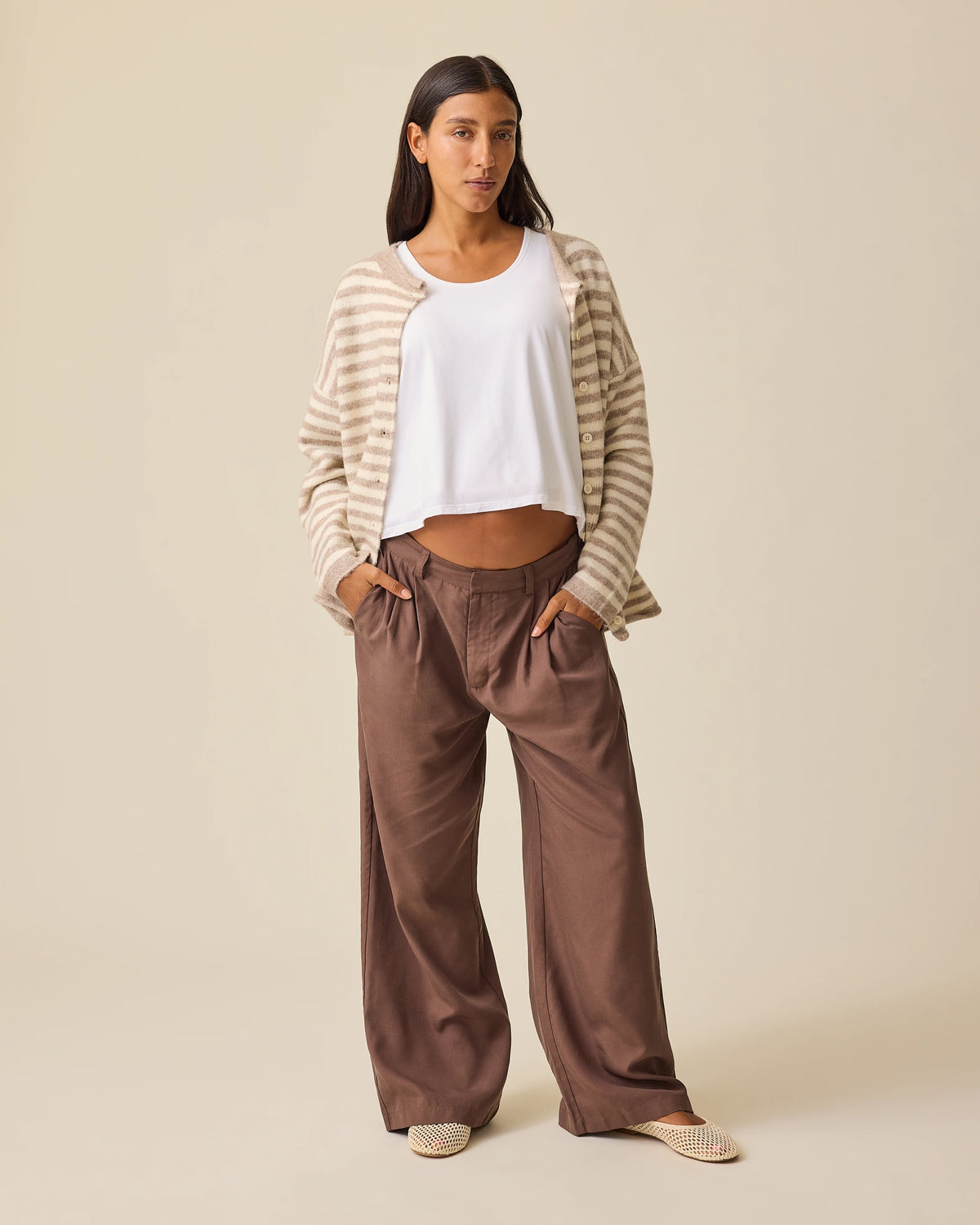 Model is wearing Ultra Soft Maternity & Postpartum Cardigan in Tan & White Stripe, Maternity & Postpartum Wide Leg Trouser in Brown and a nursing white tee, on a beige background.