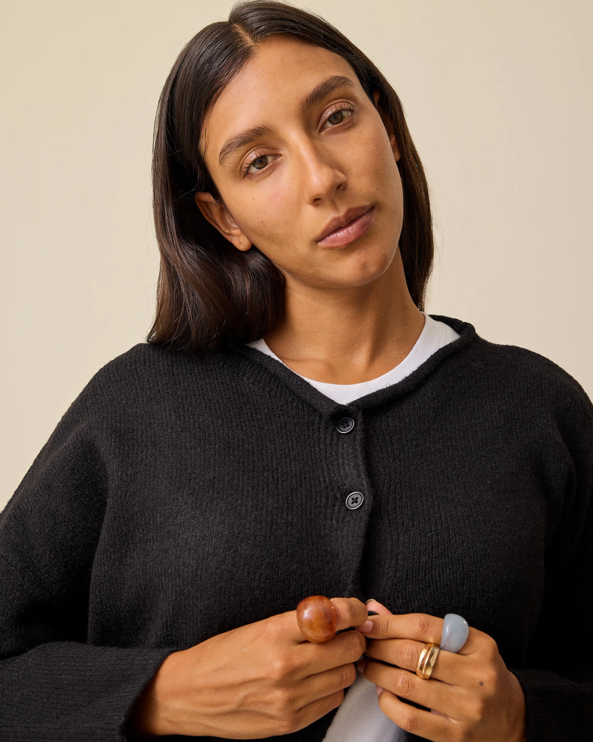 Model is buttoning up Ultra Soft Maternity & Postpartum Cardigan in Black, Wide Leg Maternity & Postpartum Jean in Medium Wash and a white nursing top, on a beige background.
