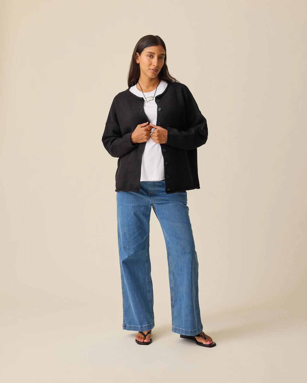 Model is wearing Ultra Soft Maternity & Postpartum Cardigan in Black, Wide Leg Maternity & Postpartum Jean in Medium Wash and a white nursing top, on a beige background.