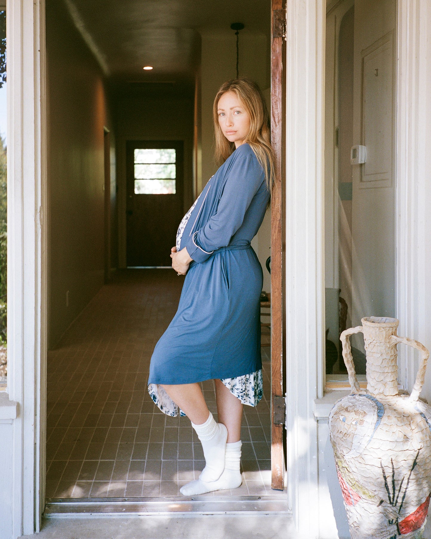 Model wearing Clea Bamboo Robe in Slate Blue in doorway to home hallway