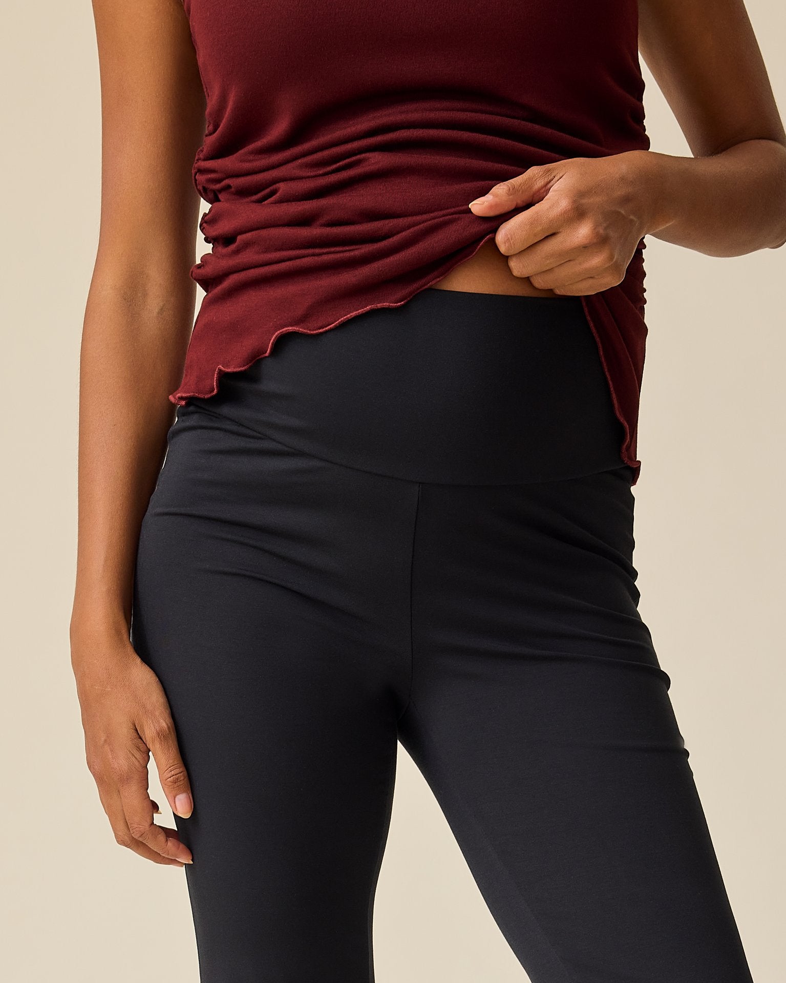 Front view of model wearing unfolded waist on the Bamboo Flex Maternity & Postpartum Flare Pant in Black on a beige background.