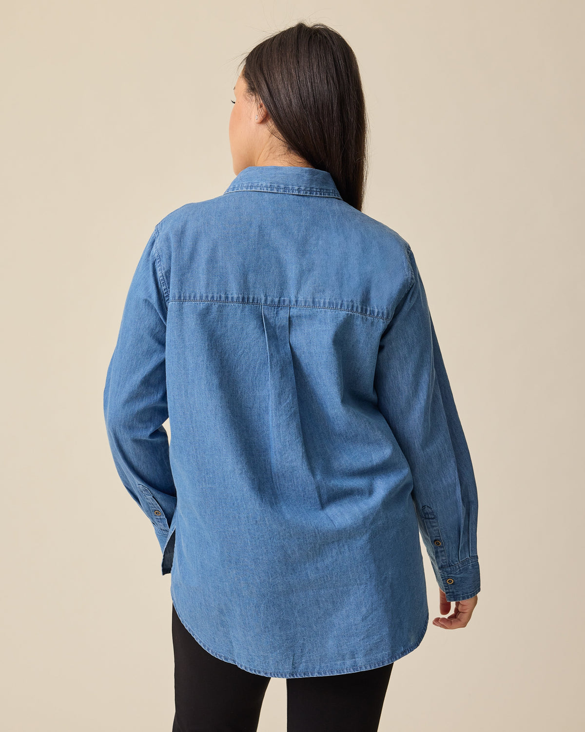 Back view of model wearing Denim Maternity & Nursing Button Up Shirt in Medium Wash and Maternity Ponte Straight Leg Pant in Black on a beige background.