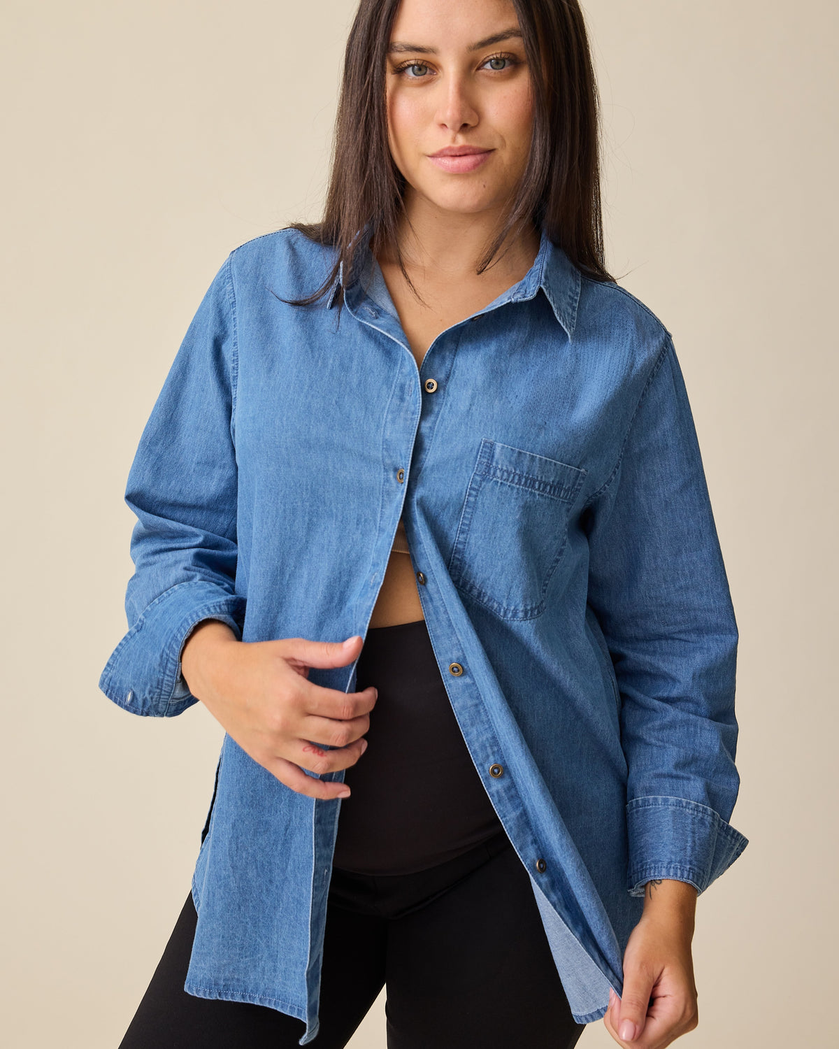 Model is wearing Denim Maternity & Nursing Button Up Shirt in Medium Wash and Maternity Ponte Straight Leg Pant in Black on a beige background.