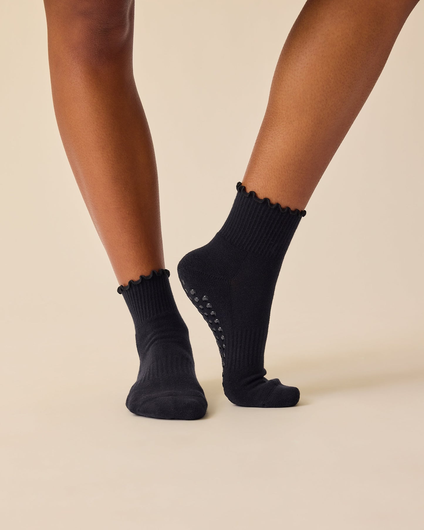 Model is wearing Non-Slip Ruffle Ankle Socks in Black on a beige background.