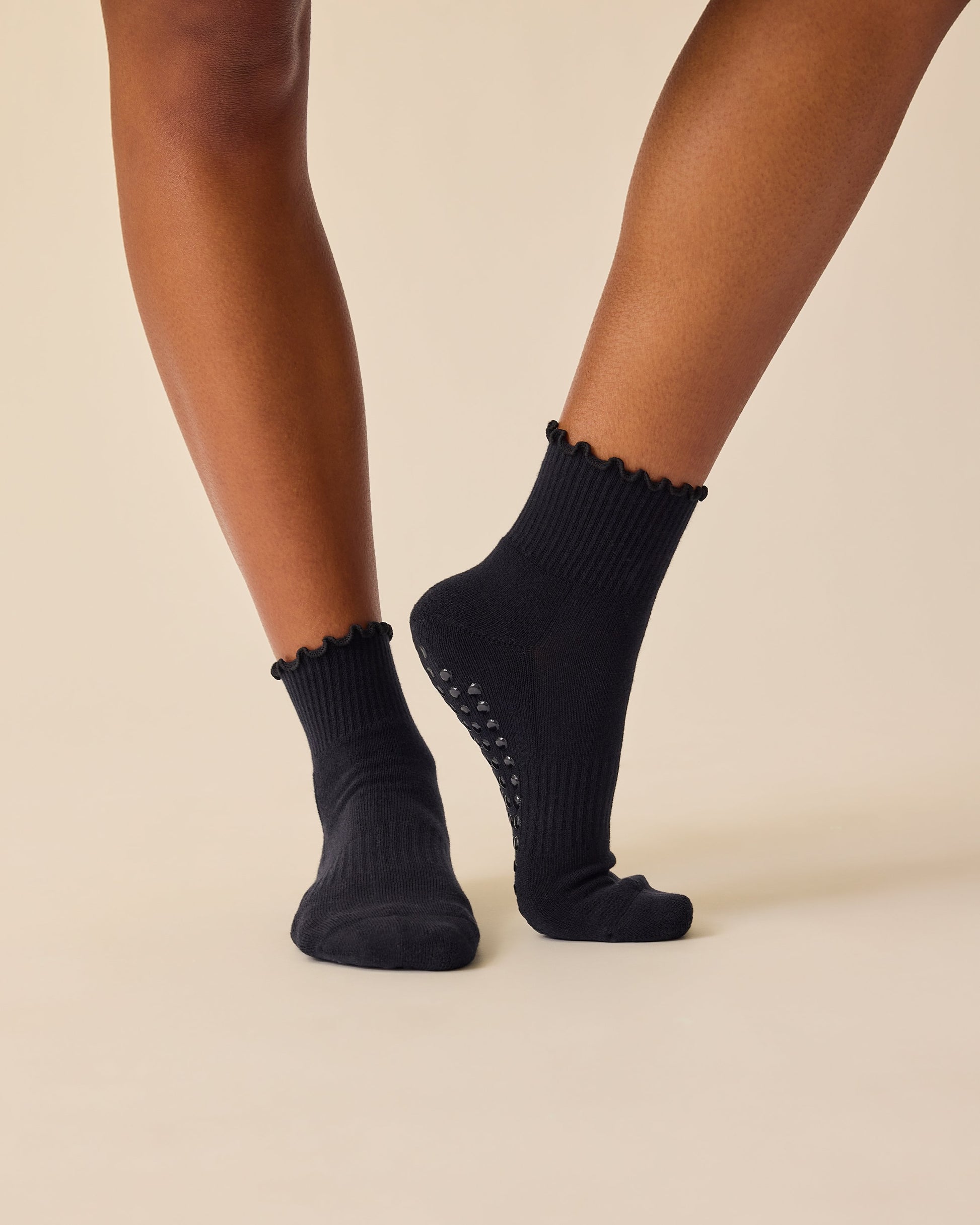 Model is wearing Non-Slip Ruffle Ankle Socks in Black on a beige background.