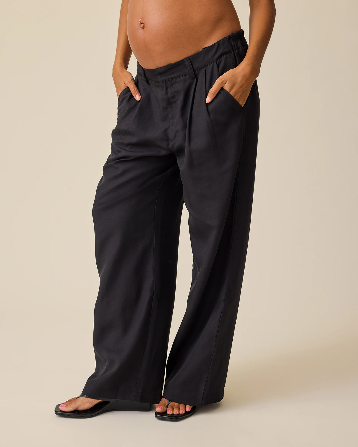 Side view of model wearing Maternity & Postpartum Wide Leg Trouser in Black on a beige background.