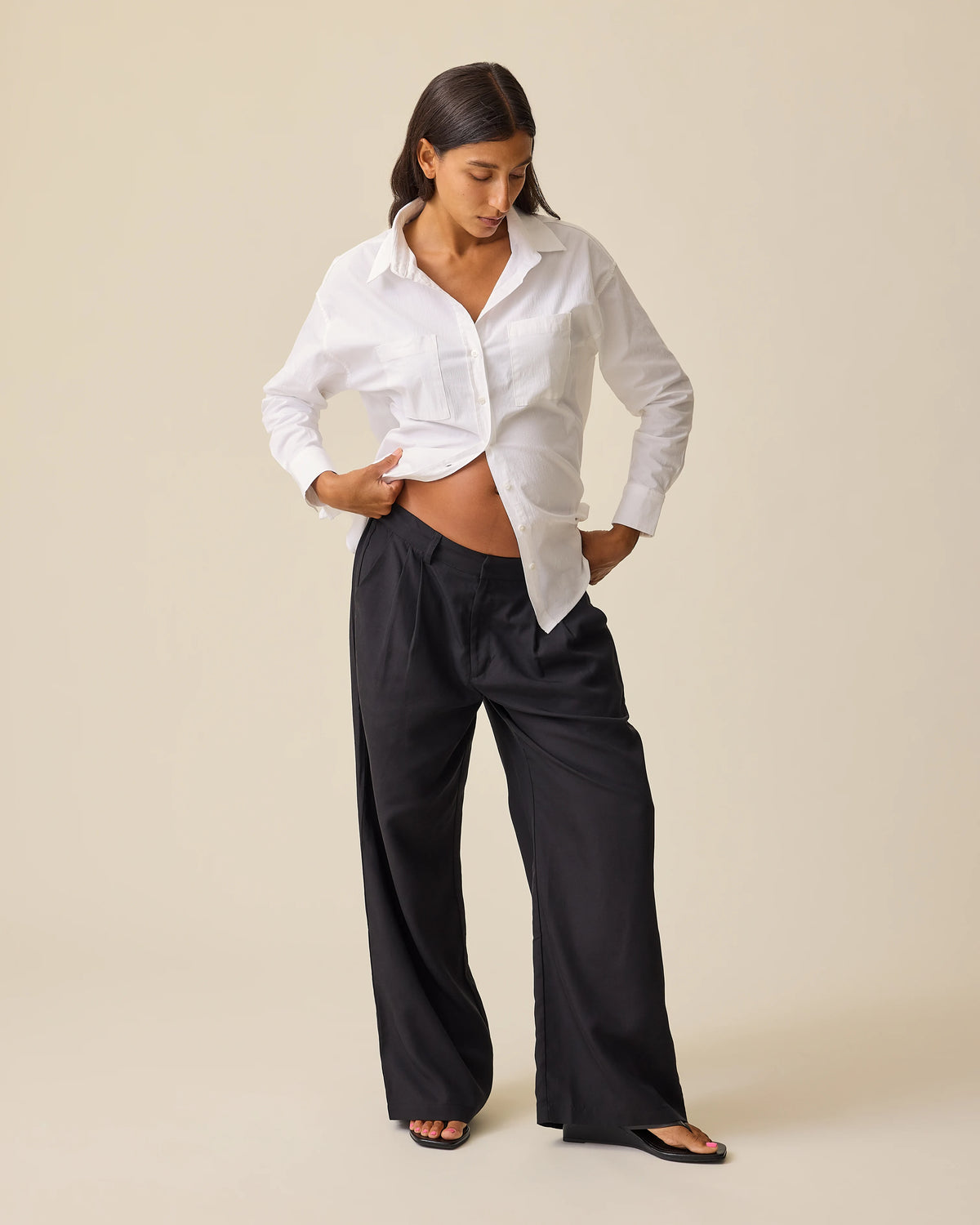 Model is wearing Maternity & Postpartum Wide Leg Trouser in Black and white Poplin Maternity & Nursing Button Up Shirt, on a beige background.