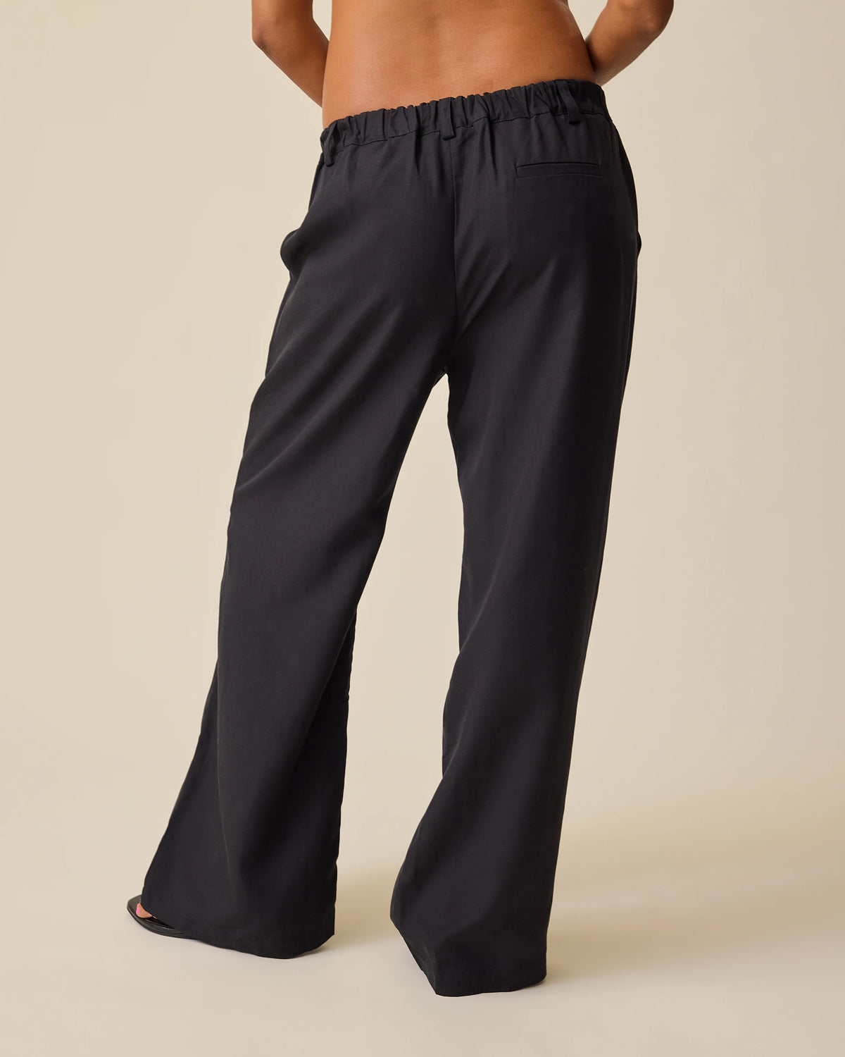 Back view of model wearing Maternity & Postpartum Wide Leg Trouser in Black on a beige background.