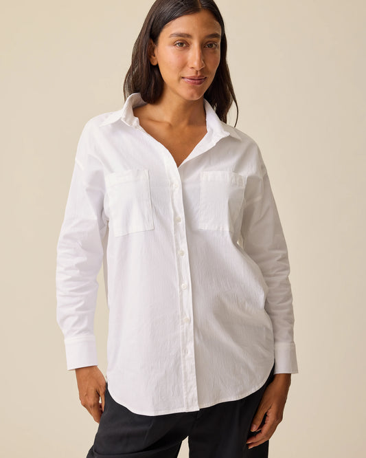Woman wearing the white Poplin Maternity & Nursing Button Up Shirt with black pants, against a solid beige background.@model_info:Hayley is wearing a Small.