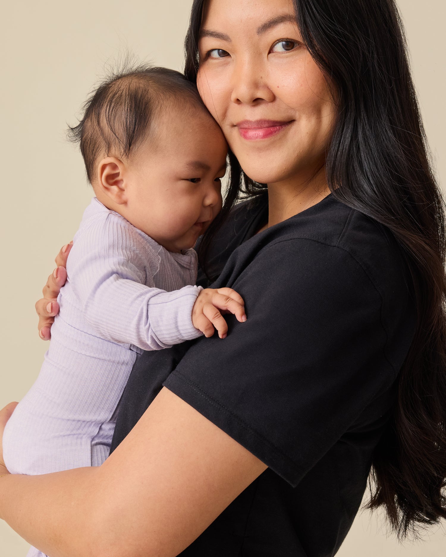 Model holding baby and wearing Relaxed Cotton Maternity & Nursing T-shirt in Black on a beige background.
