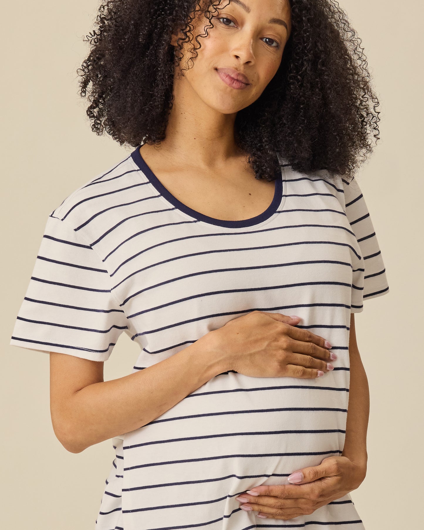 Model is wearing Relaxed Cotton Maternity & Nursing T-shirt in Navy & White Stripe on a beige background. 