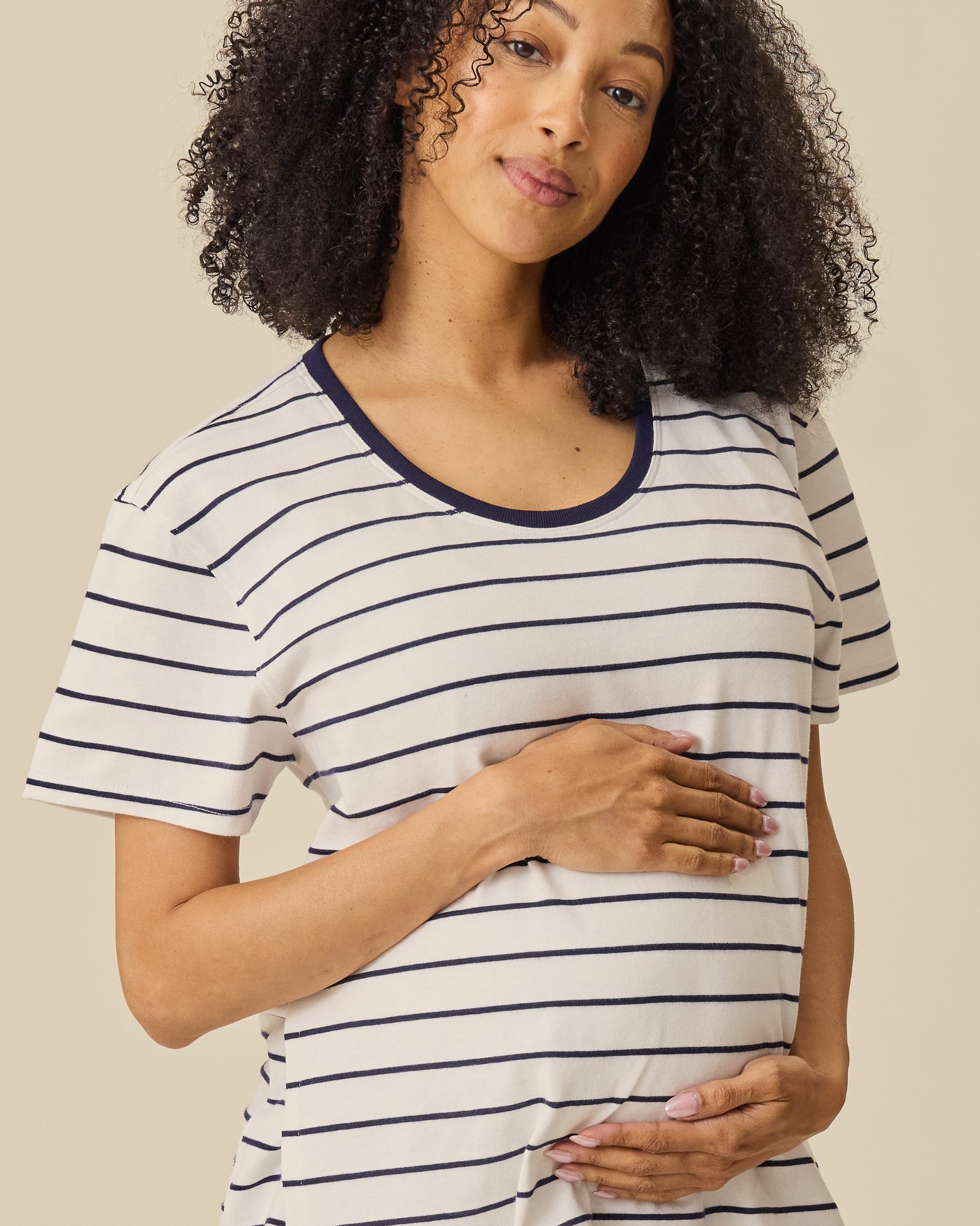 Model is wearing Relaxed Cotton Maternity & Nursing T-shirt in Navy & White Stripe on a beige background. 