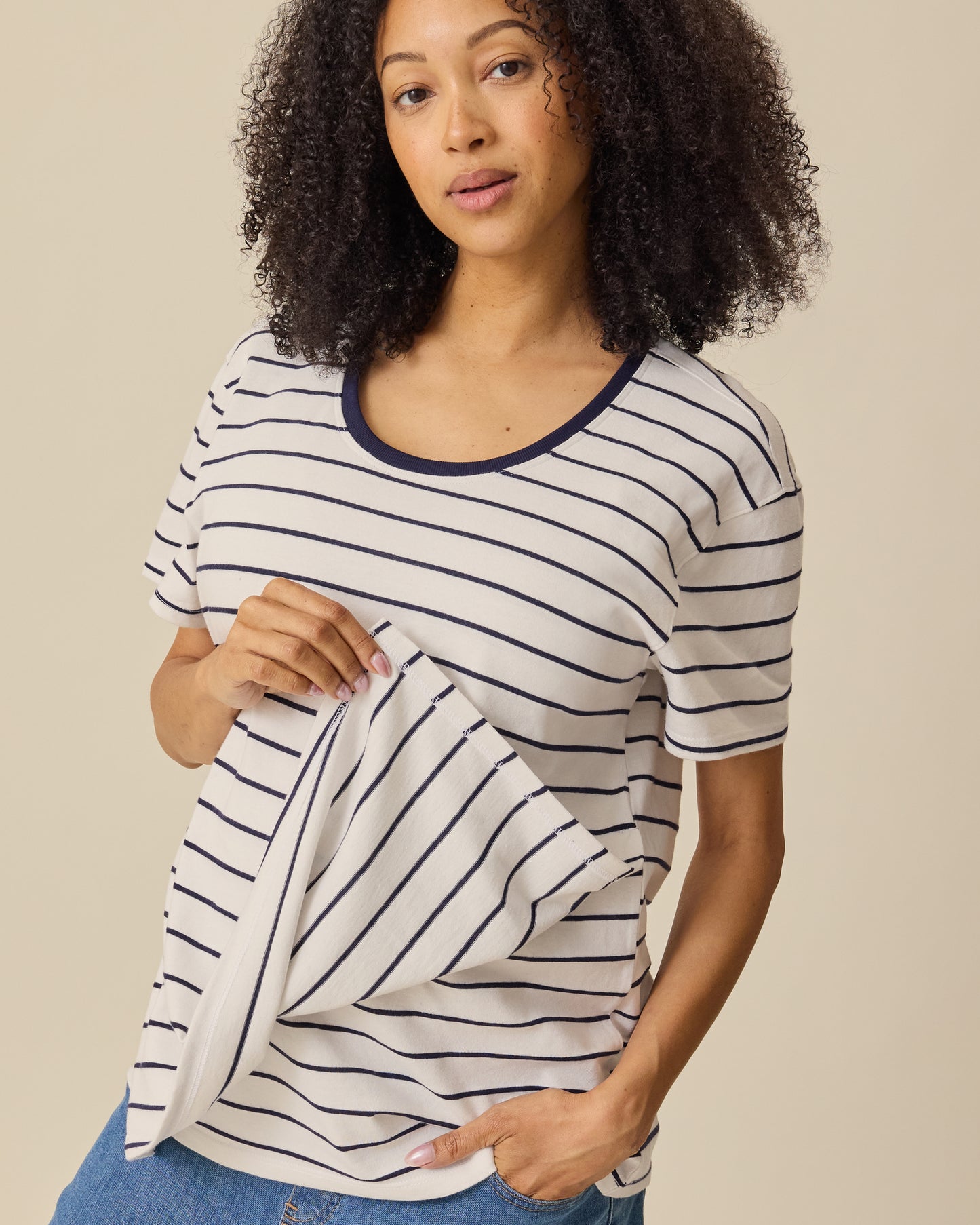 Model is showing nursing access on the Relaxed Cotton Maternity & Nursing T-shirt in Navy & White Stripe on a beige background. 