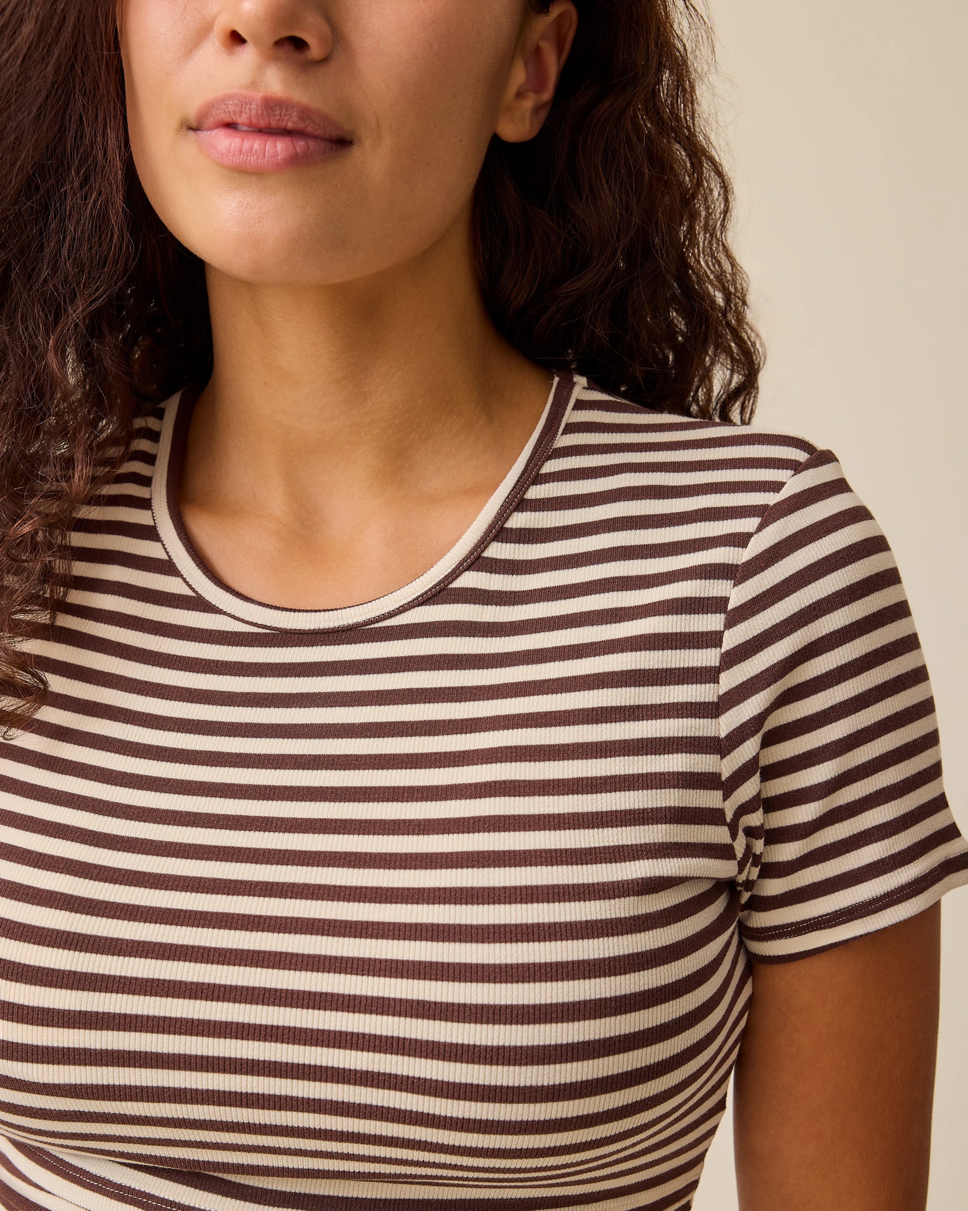 Close up of collar on the Ribbed Bamboo Crew Neck Nursing T-shirt in Chocolate & Ivory Stripe on a beige background.