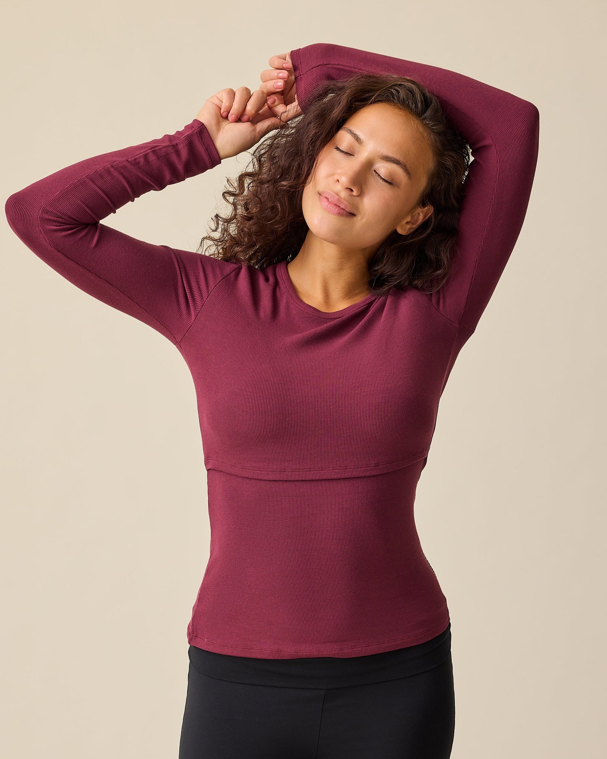Model is wearing Ribbed Bamboo Long Sleeve Nursing T-shirt in Deep Burgundy with black pants, on a beige background.