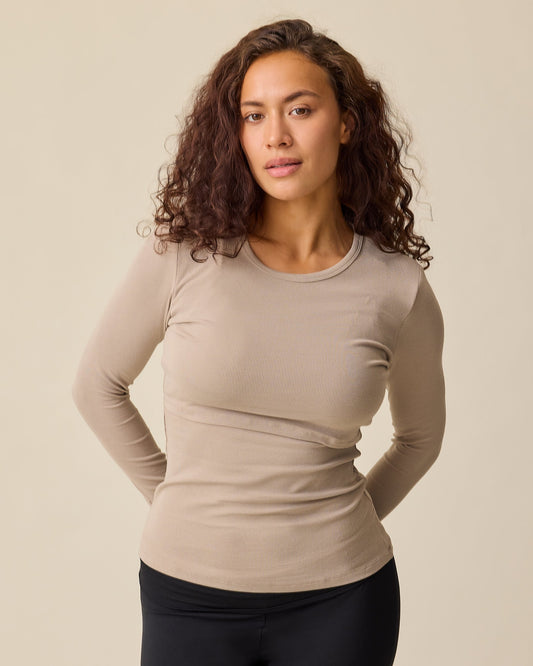Model is wearing the Ribbed Bamboo Long Sleeve Nursing T-shirt in Sandstone on a beige background. @model_info:Sadie is wearing a Medium.