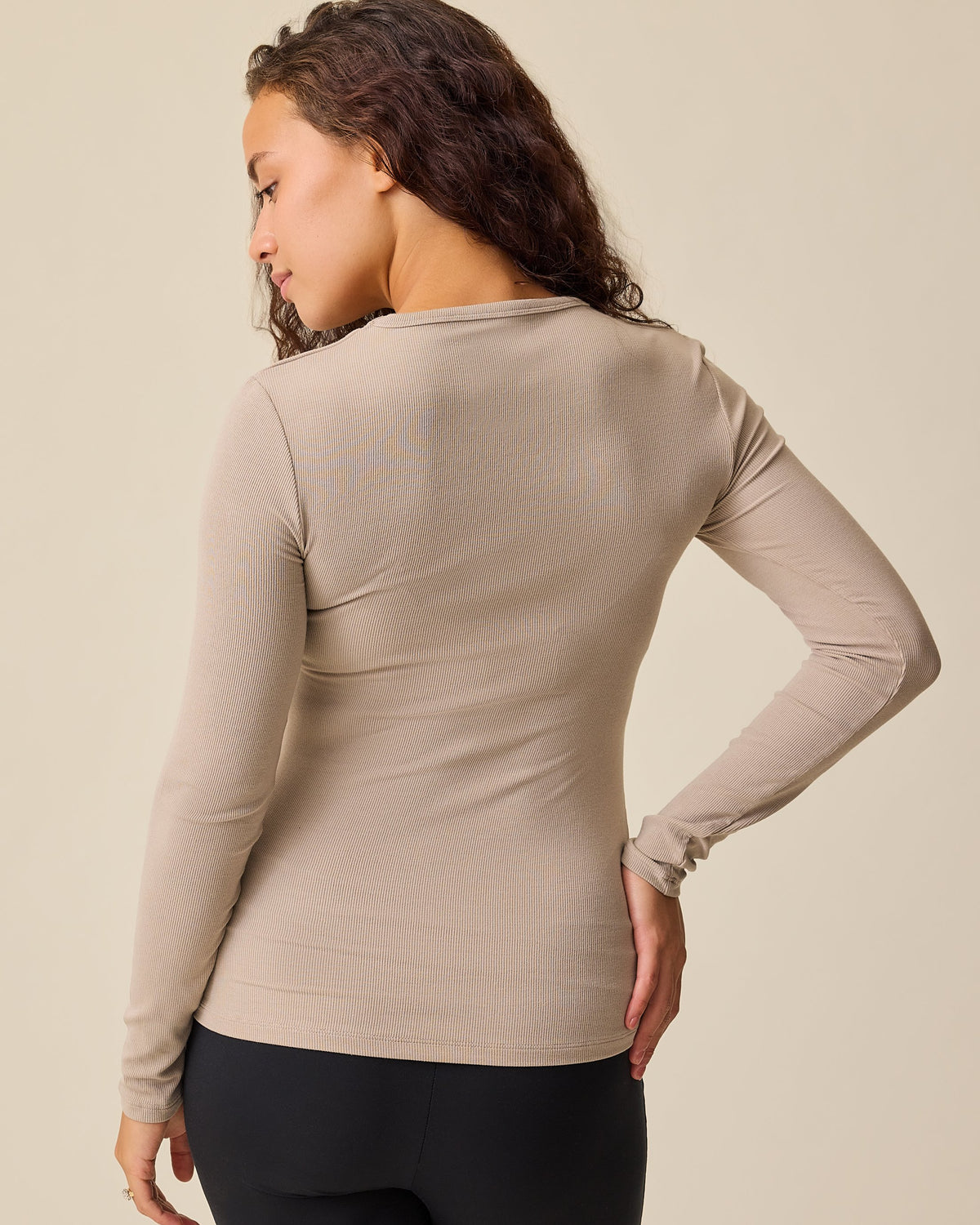 Back view of model wearing the Ribbed Bamboo Long Sleeve Nursing T-shirt in Sandstone on a beige background. 