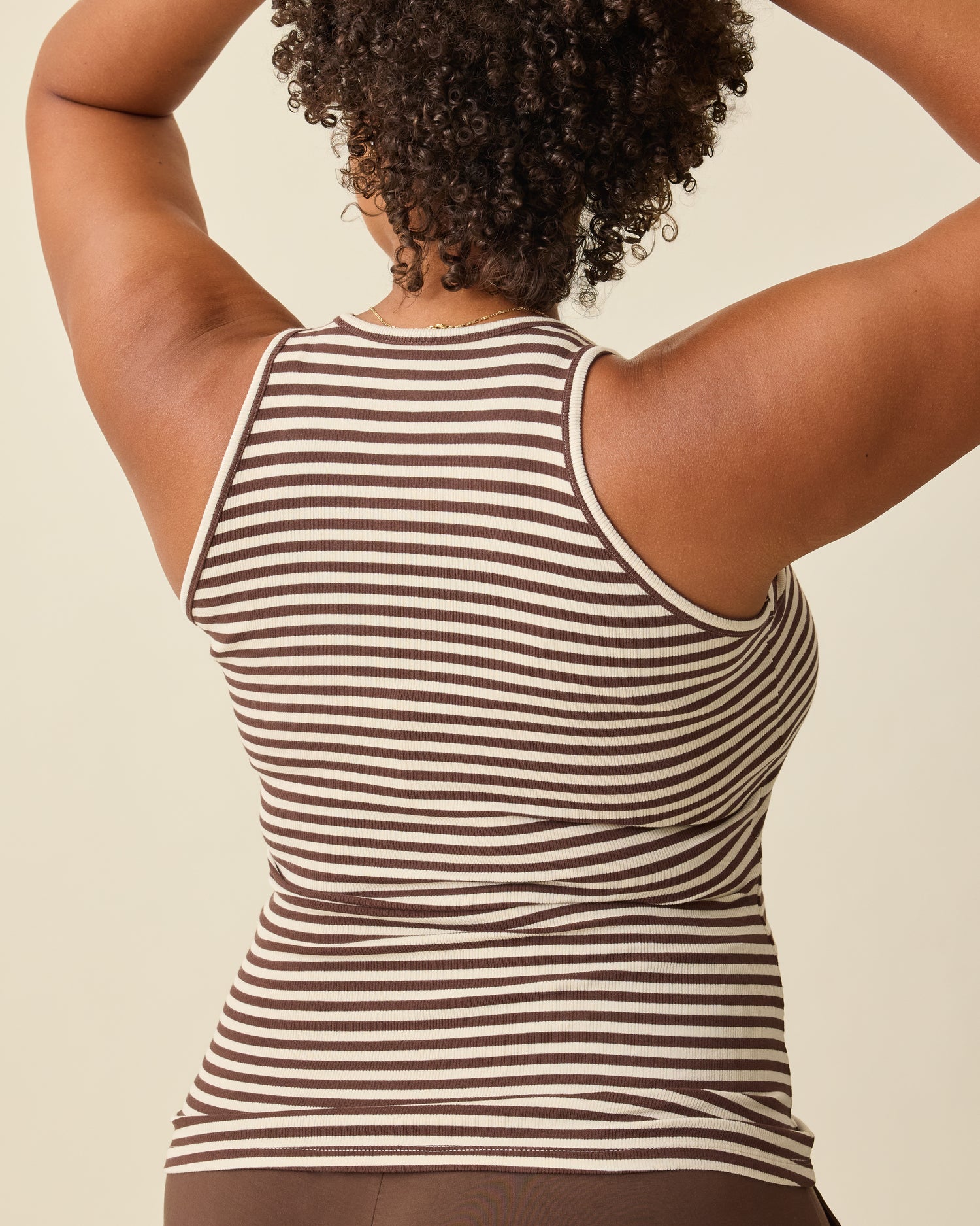 Back view of model wearing Ribbed Bamboo Racerback Nursing Tank in Chocolate & Ivory Stripe on a beige background. 