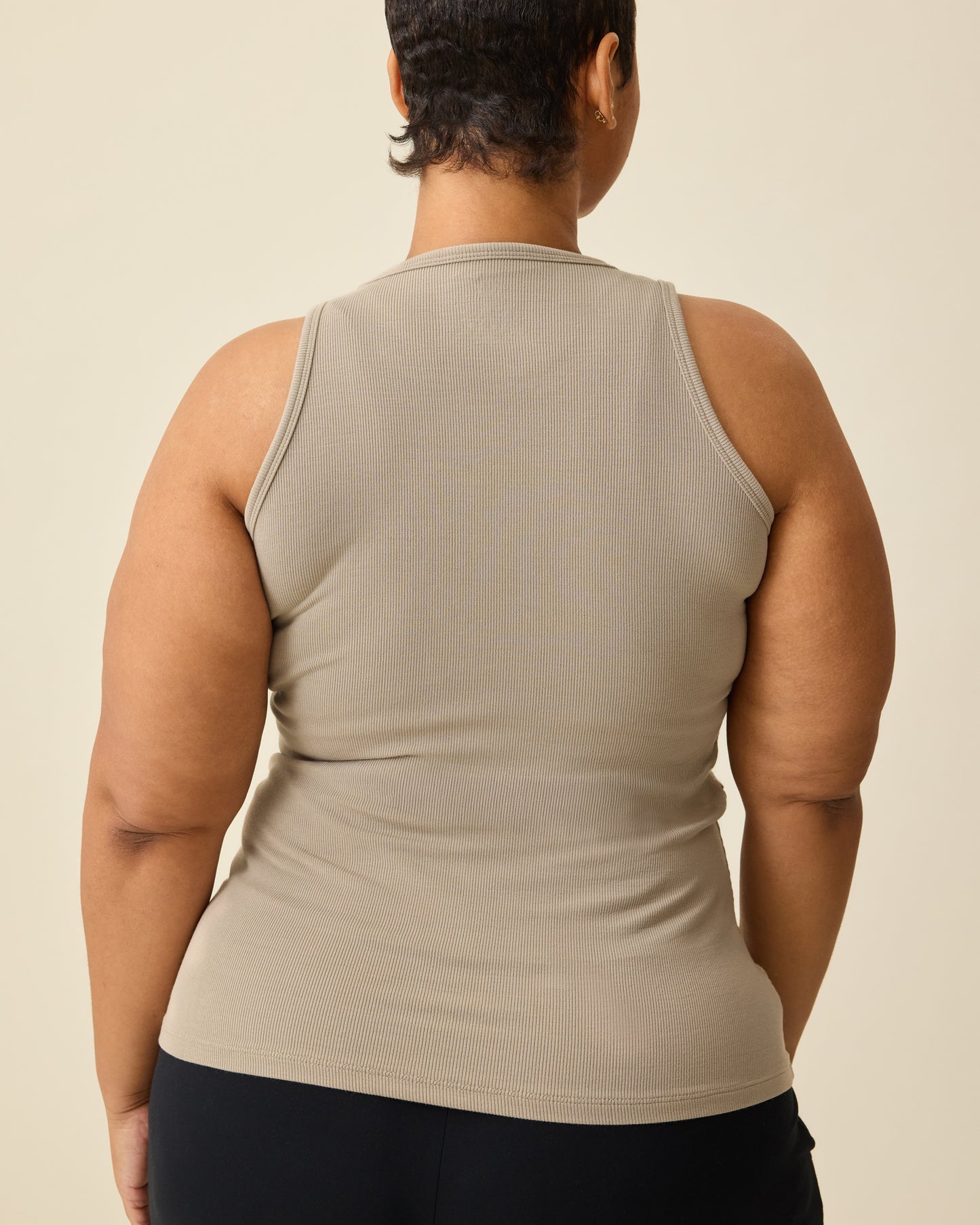 Back view of model wearing the Ribbed Bamboo Racerback Nursing Tank in Sandstone on a beige background. 