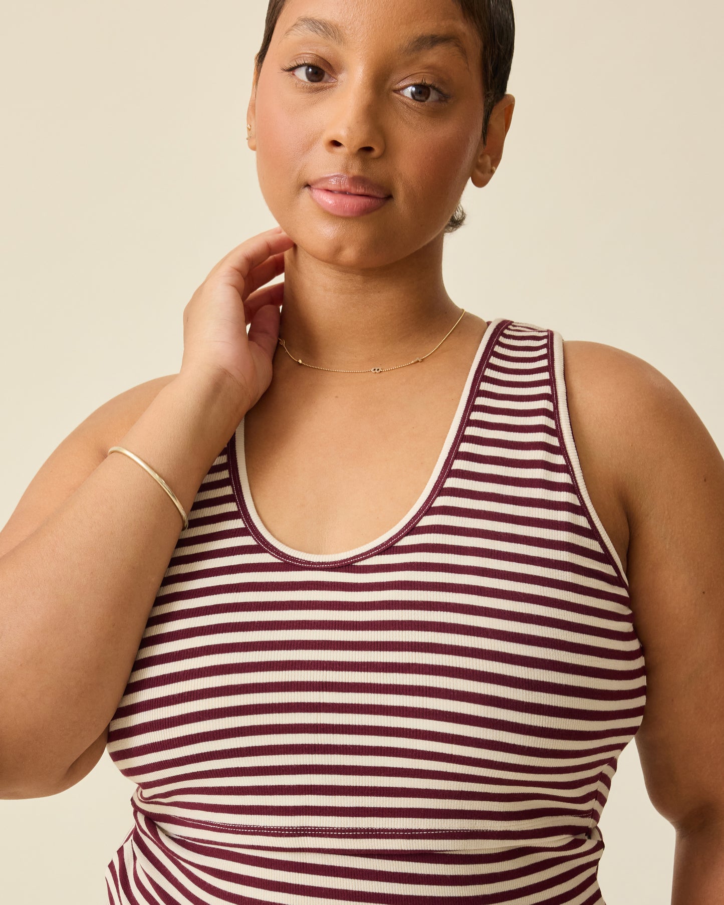 Model is wearing Ribbed Bamboo Scoop Neck Nursing Tank in Garnet Stripe on a beige background. 
