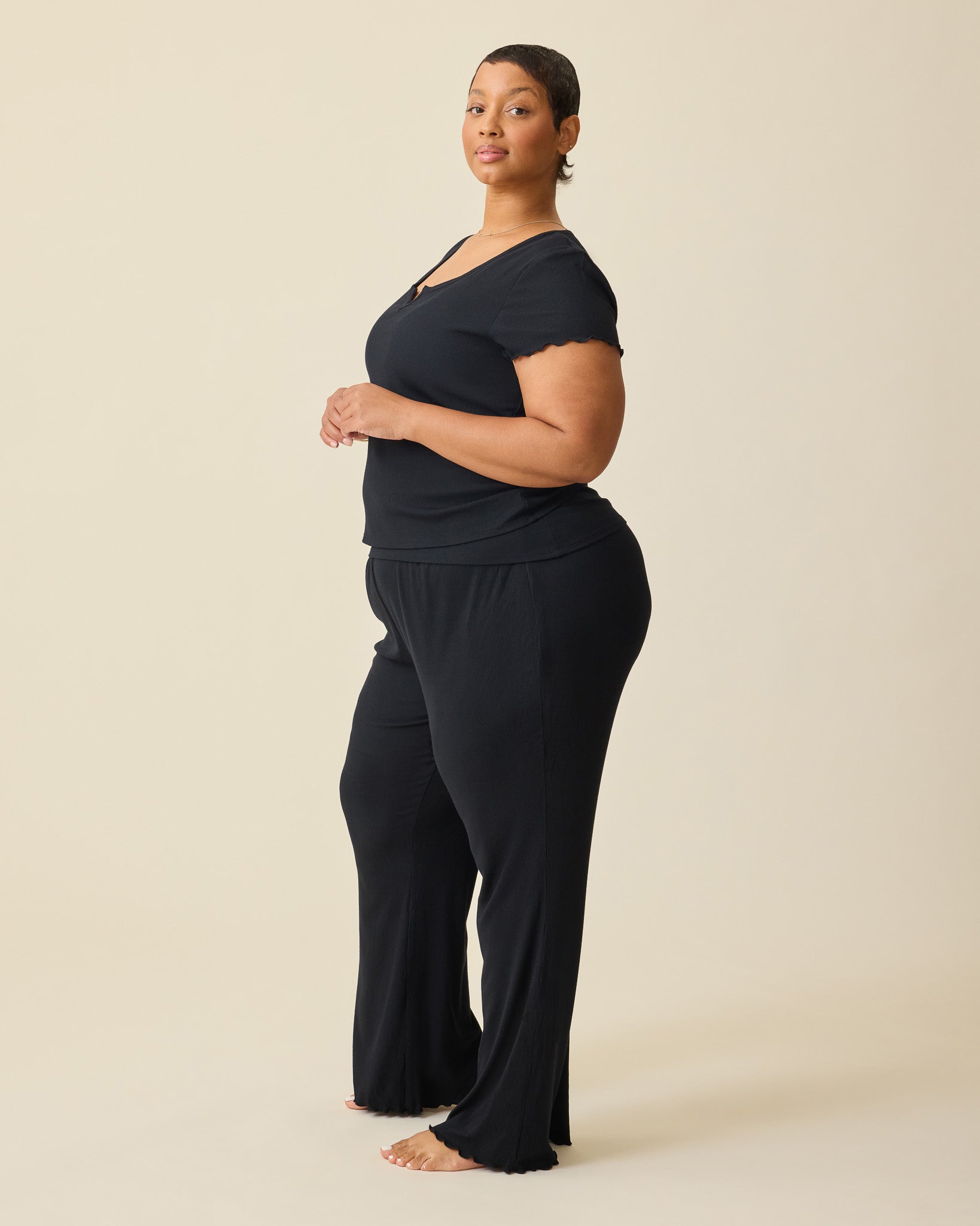 Side view of model wearing Ribbed Modal Lounge Pant in Black and Ribbed Modal Notched Nursing T-shirt in Black on a beige background.@model_info:Brittany is 5'5" and wearing a 1X.