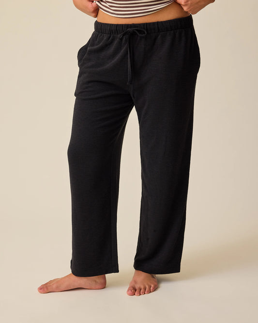Woman wearing Luxe Terry Maternity & Postpartum Pant in Black, on a beige background.@model_info:Sadie is 5'8" and wearing a Medium.