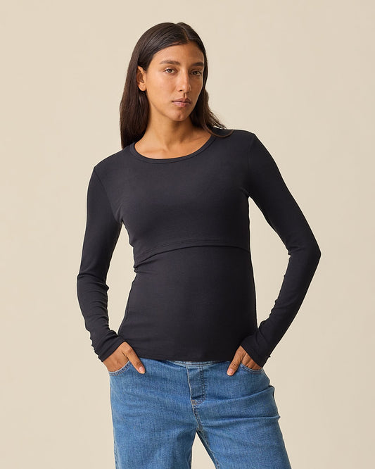 A woman wearing the Ribbed Bamboo Long Sleeve Nursing T-shirt in Black,  paired with blue jeans, against a solid beige background@model_info:Hayley is wearing a Small.