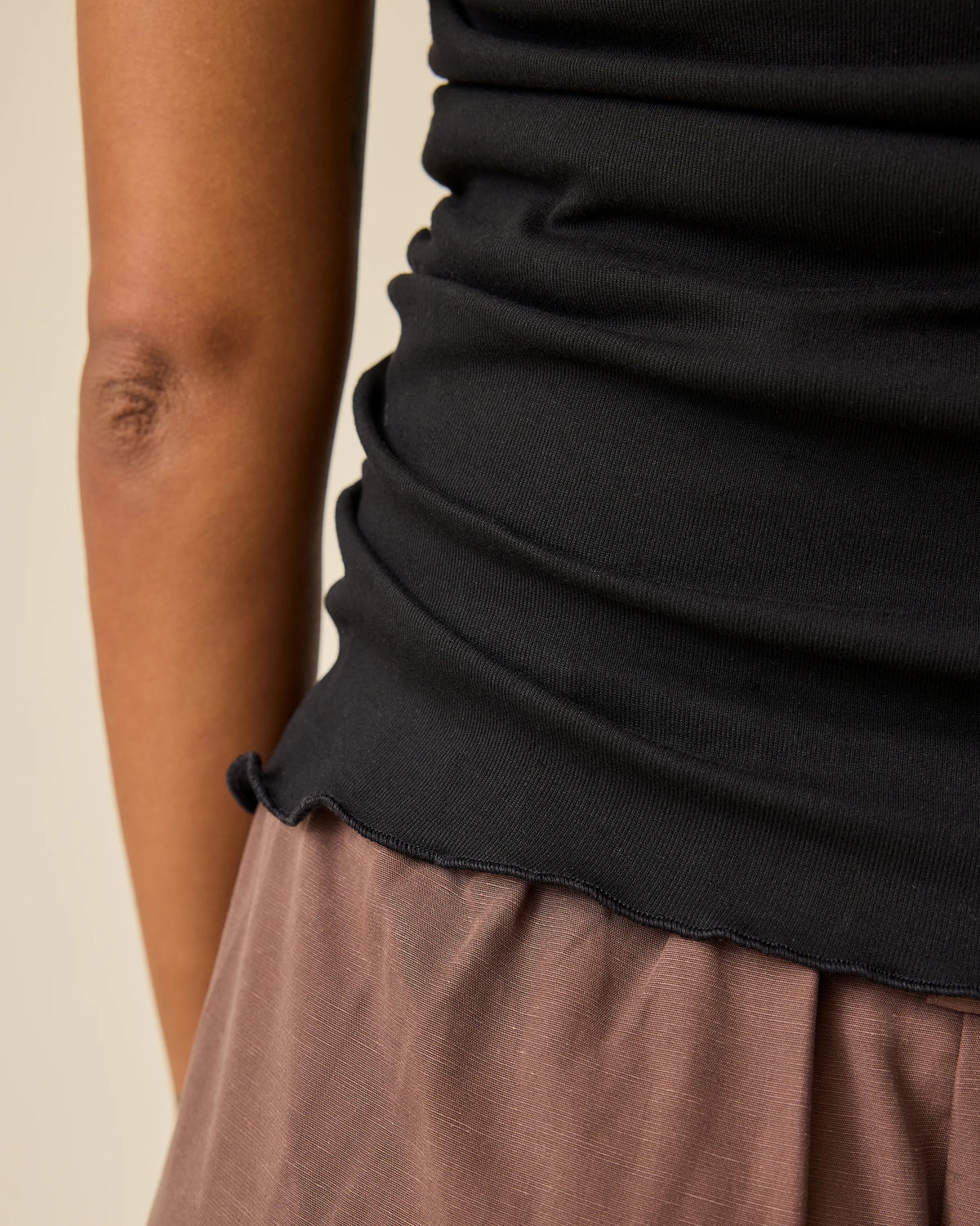 Close up of Maternity & Postpartum Wide Leg Trouser in Brown and Ruched Maternity Sleeveless Top in Black on a beige background.