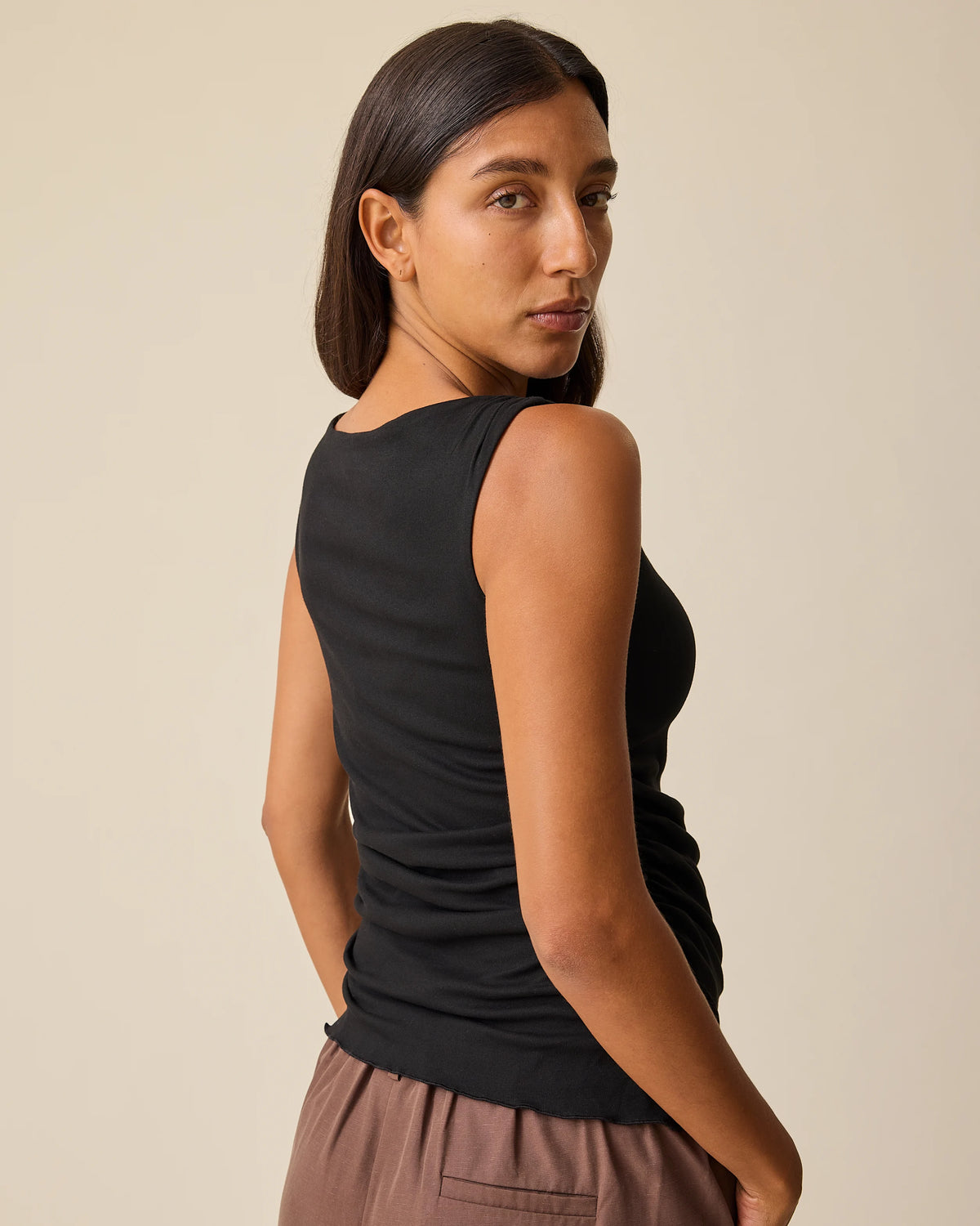 Side view of Maternity & Postpartum Wide Leg Trouser in Brown and Ruched Maternity Sleeveless Top in Black on a beige background.