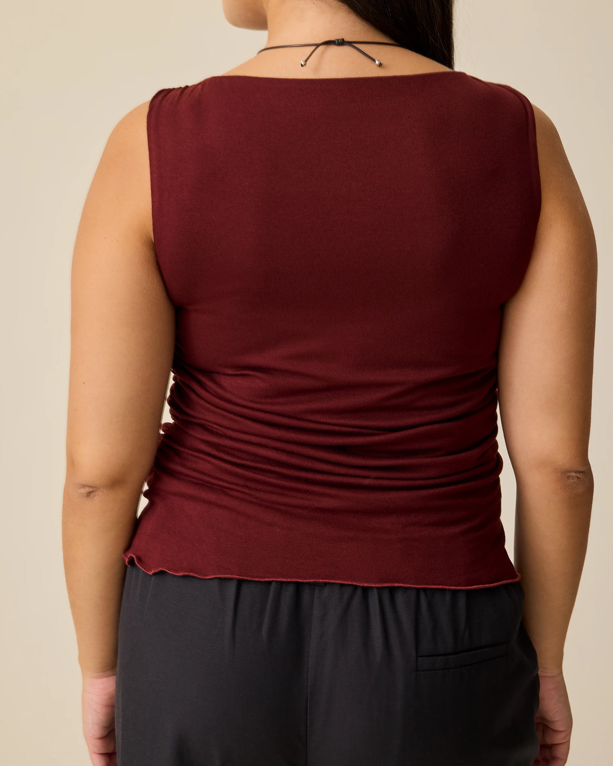 Back view of model wearing Ruched Maternity Sleeveless Top in Burgundy and Maternity & Postpartum Wide Leg Trouser in Black on a beige background. 