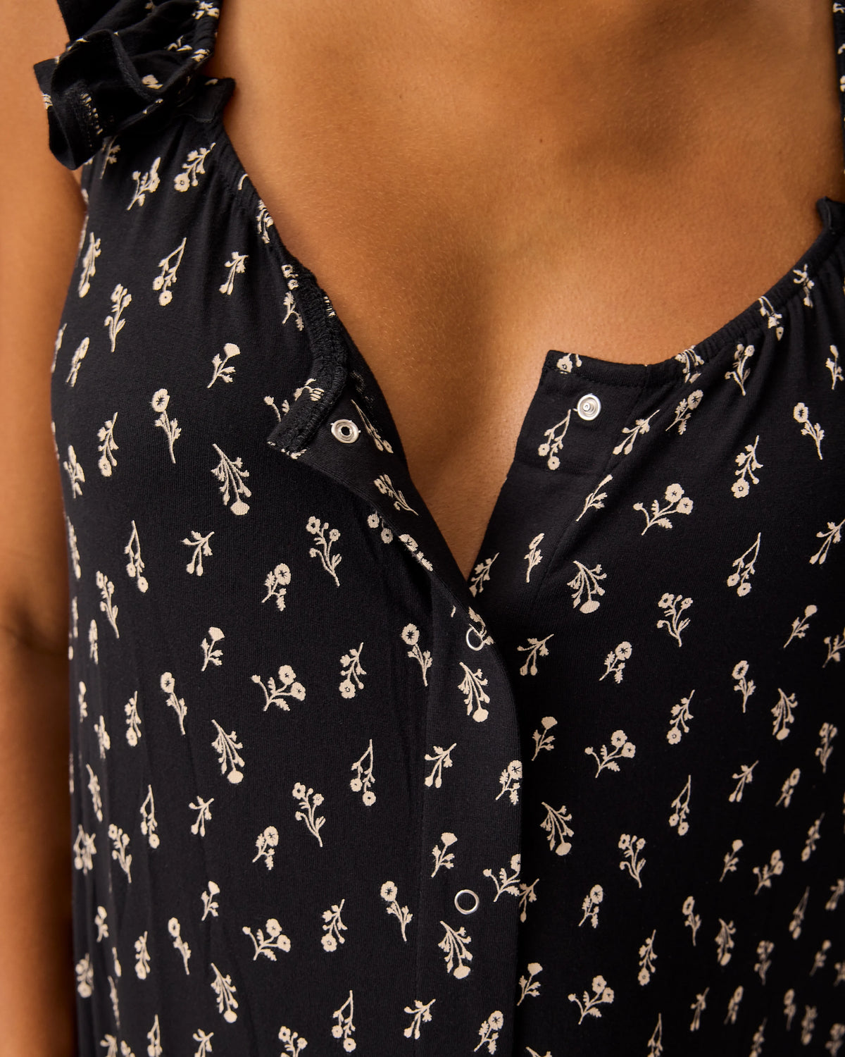 Close up of model wearing Ruffle Strap Labor & Delivery Gown in Black Wildflower on a beige background. 