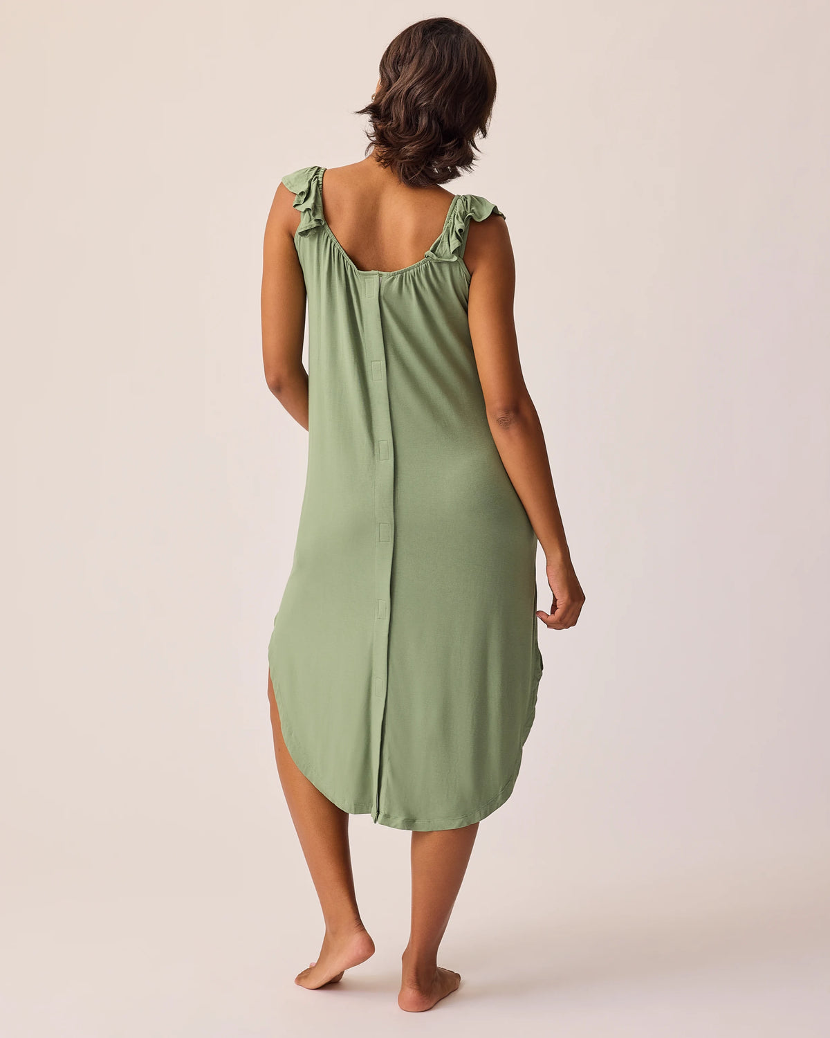 Back view of the model wearing Ruffle Strap Labor & Delivery Gown in Sage on a beige background.