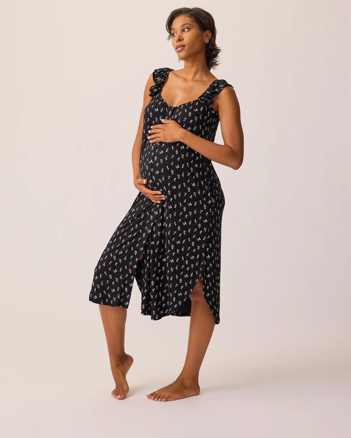 Model is wearing Ruffle Strap Labor & Delivery Gown in Black Wildflower on a beige background. @model_info:Ale is 5'9" and wearing a M/L.