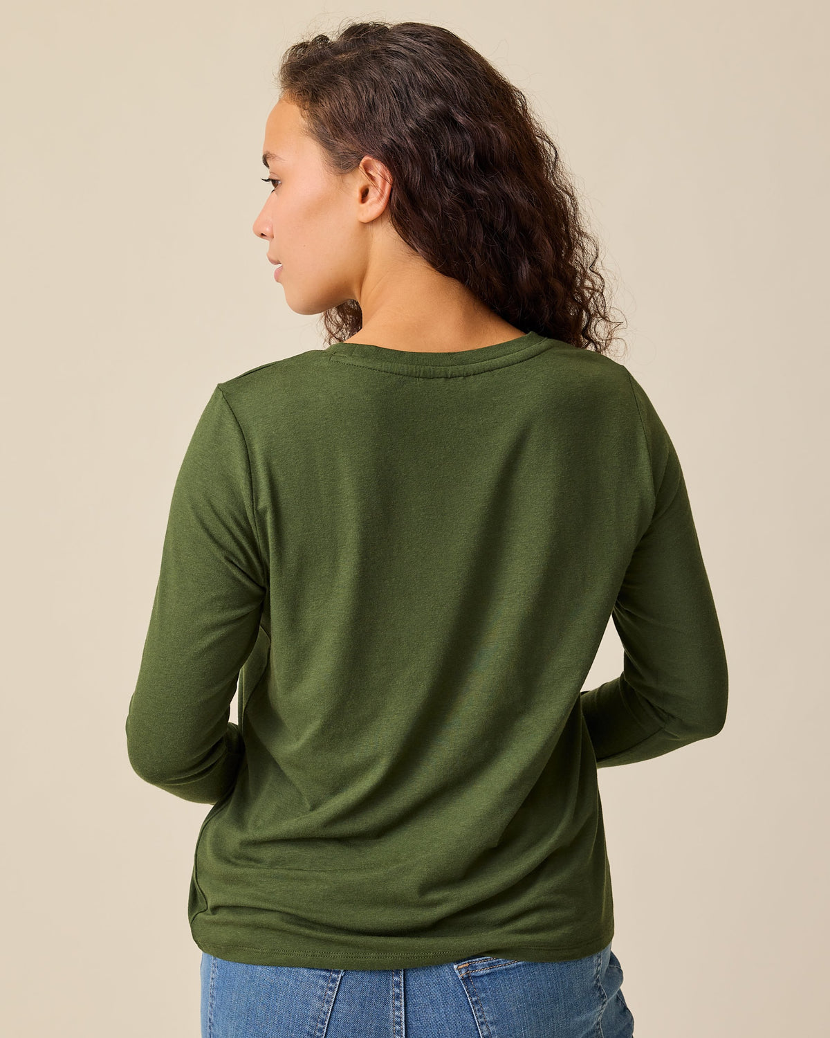 Back view of model wearing Modal Long Sleeve Nursing T-shirt in Deep Olive and Wide Leg Maternity & Postpartum Jean in Medium Wash on a beige background.