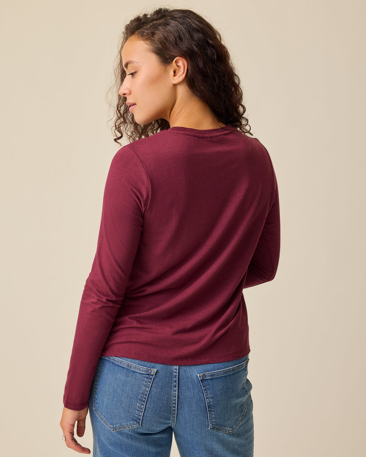 Back view of model wearing Modal Long Sleeve Nursing T-shirt in Garnet and Wide Leg Maternity & Postpartum Jean in Medium Wash on a beige background.