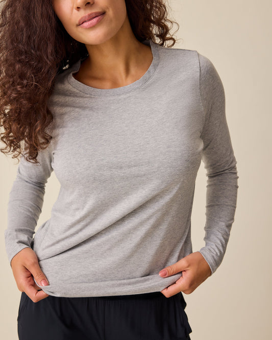 Model is adjusting the soft material of the Modal Long Sleeve Nursing T-shirt in Grey Heather on a beige background.@model_info:Sadie is wearing a Medium.