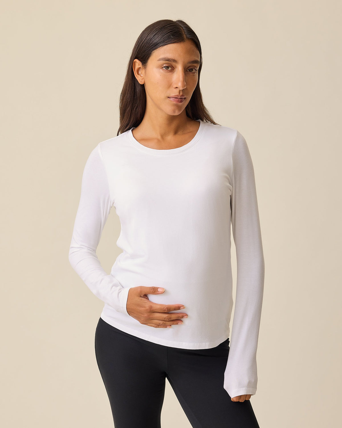 Pregnant model is wearing Modal Long Sleeve Nursing T-shirt in White on a beige background.@model_info:Hayley is wearing a Small.