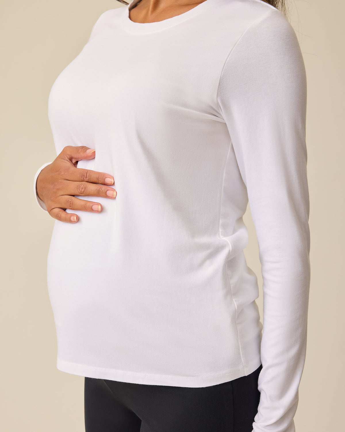 Angled view of pregnant model is wearing Modal Long Sleeve Nursing T-shirt in White on a beige background.