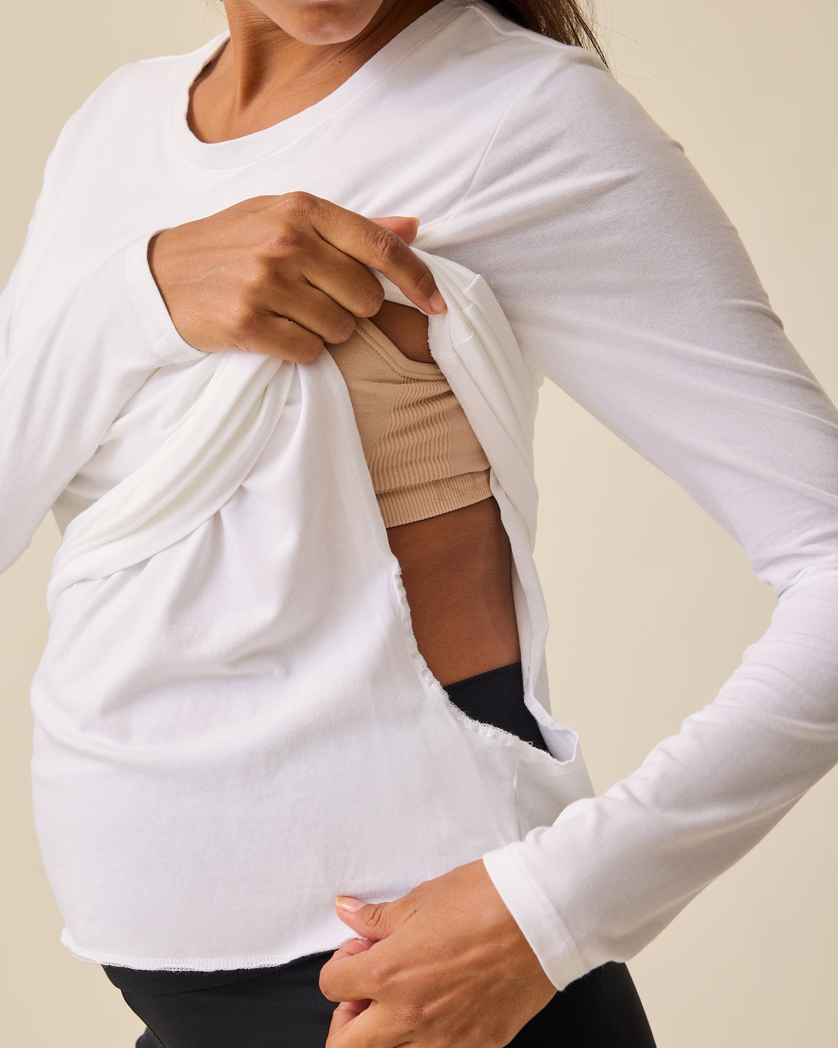 Model is lifting front panel to display the ease of nursing access with the Modal Long Sleeve Nursing T-shirt in White on a beige background.