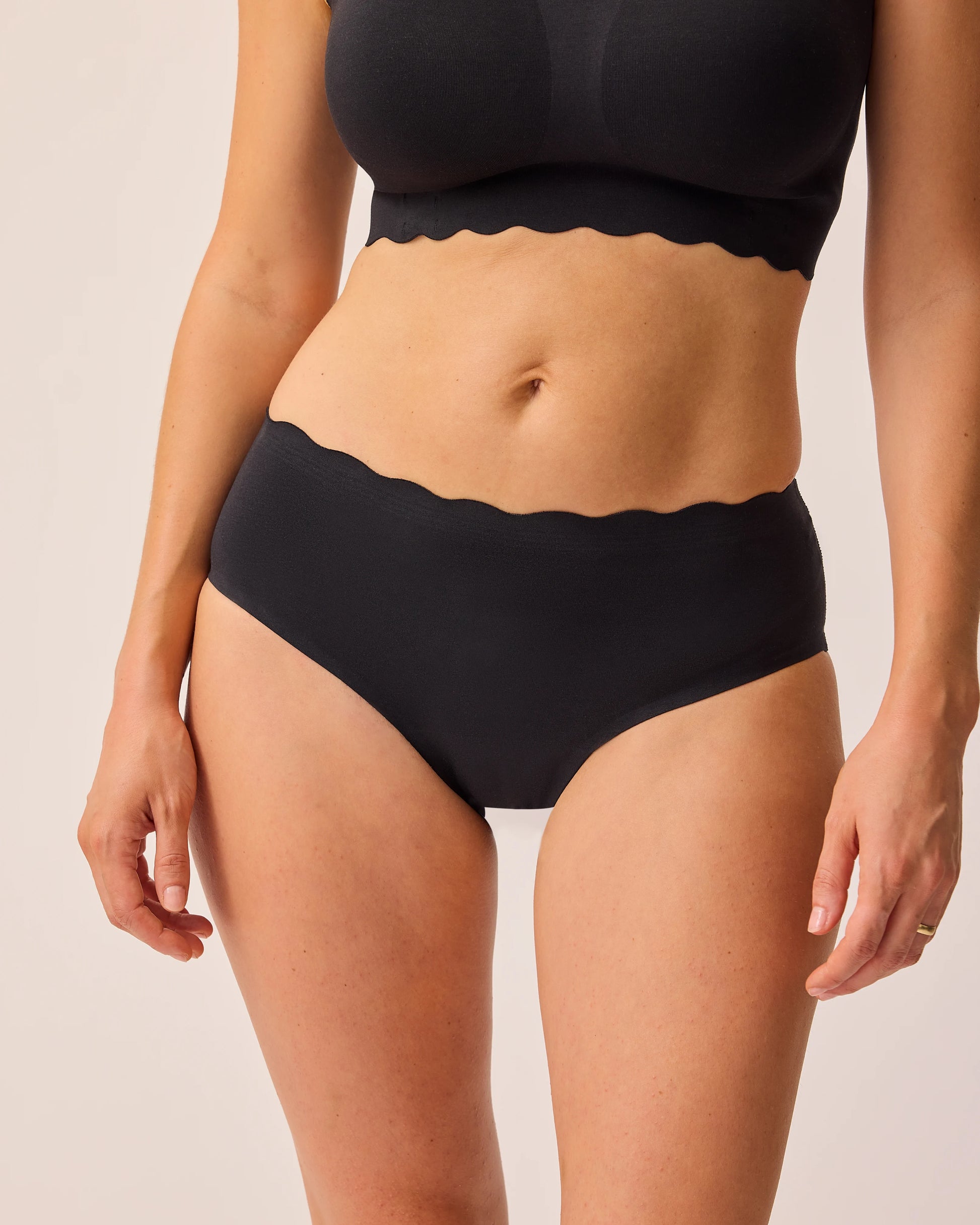 Model is wearing BareBond™ Cotton Maternity & Postpartum Brief in Black and BareBond™ Cotton Maternity & Nursing Bra in Black on a beige background. @model_info:KJ is wearing a Medium.